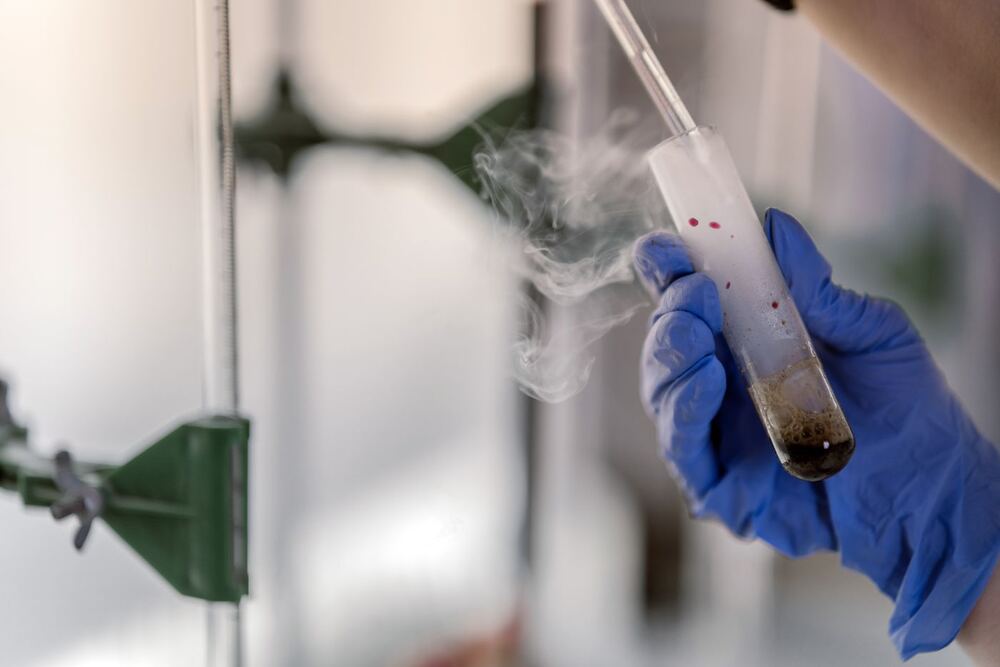 Gloved hand holding a test tube with cold vapour in a laboratory